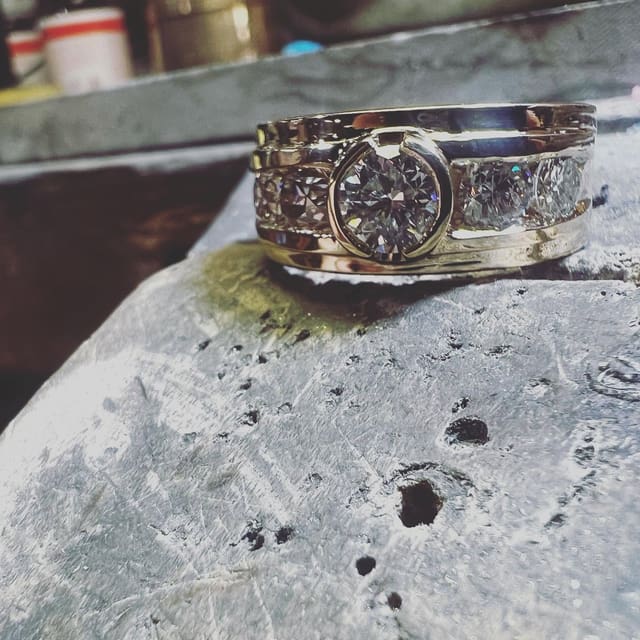The ring with its stones set, photographed close up with the bench and tools behind it.